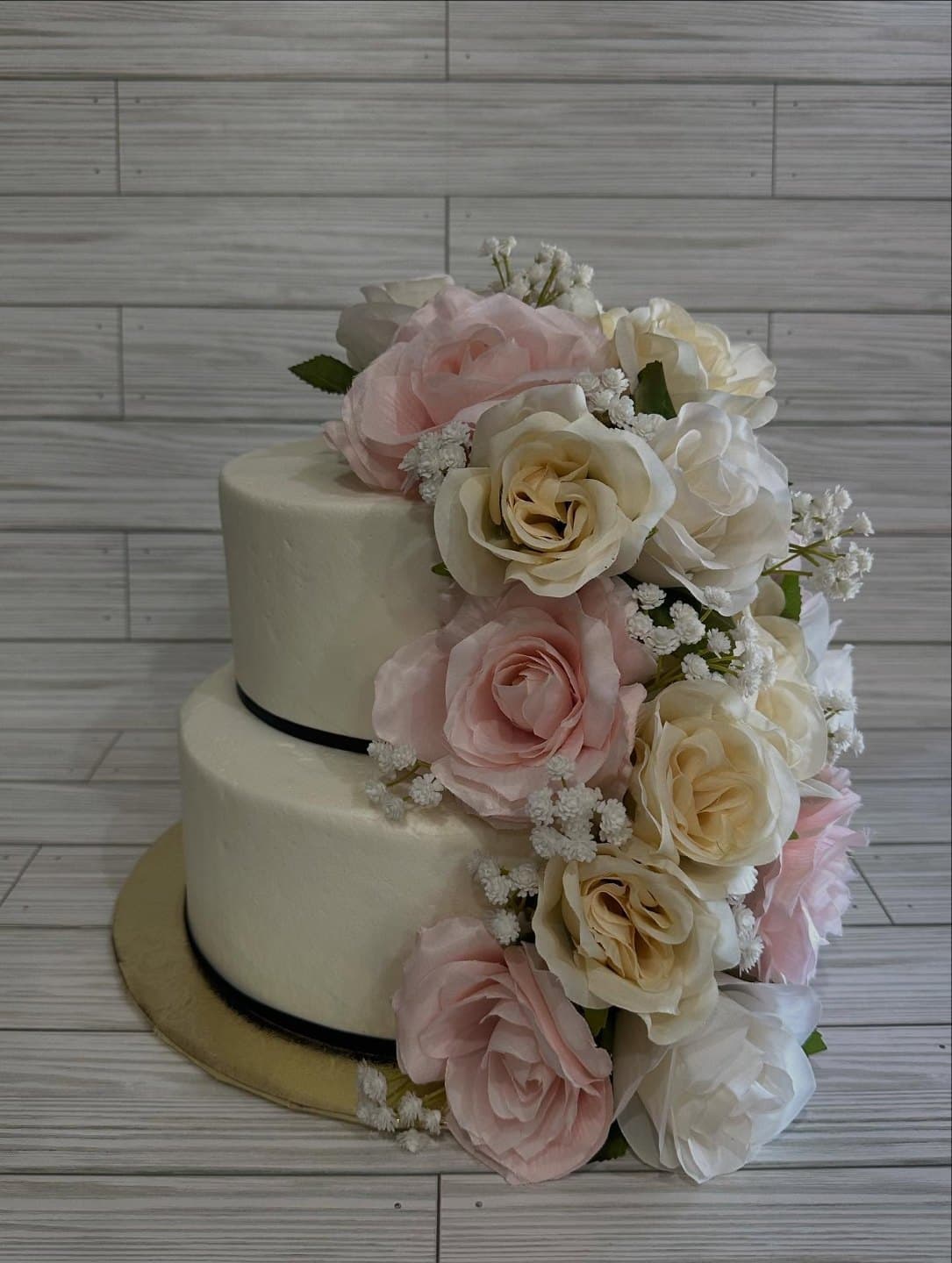 Two-tier white wedding cake with a black ribbon base and a cascade of blush and ivory roses