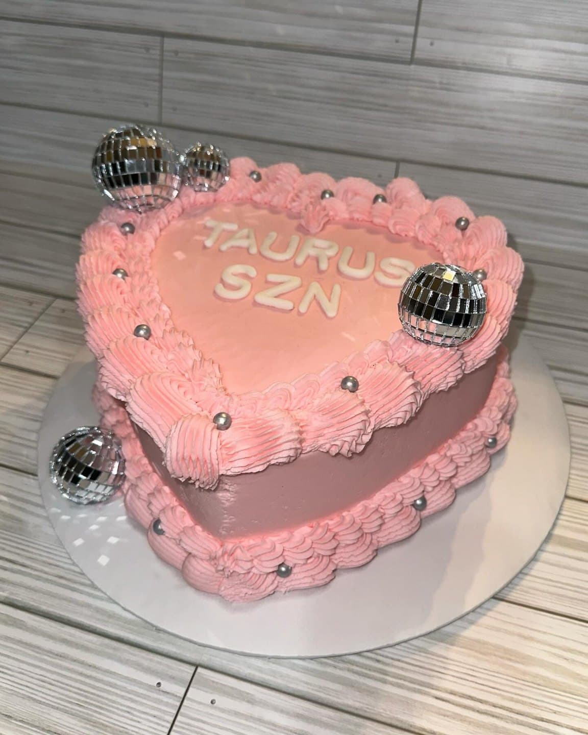 A pink heart-shaped cake piped with vintage buttercream frills, sugar pearls and mini disco balls