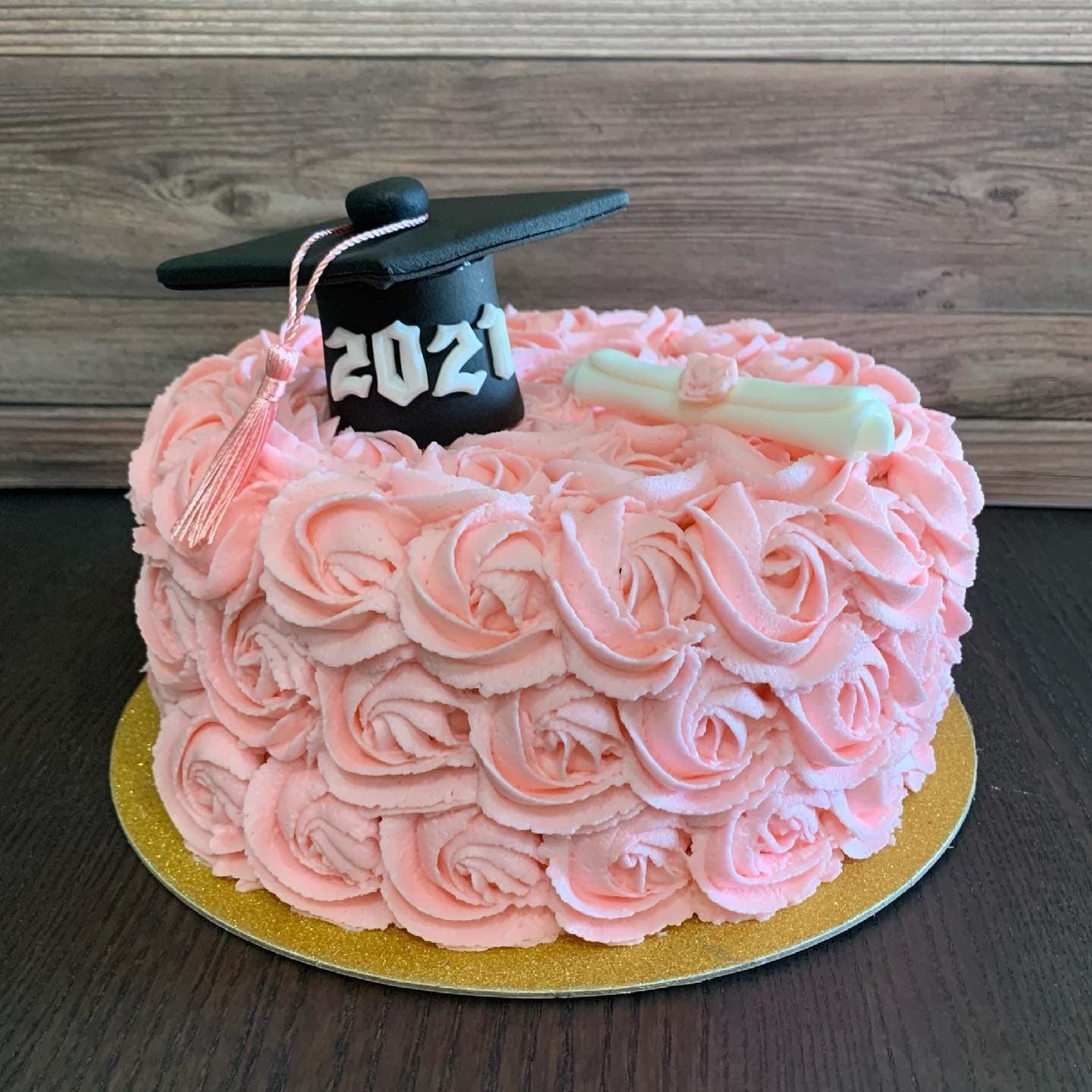 Pale-pink buttercream rosette cake on a gold board, topped with a black graduation cap and pink tassel