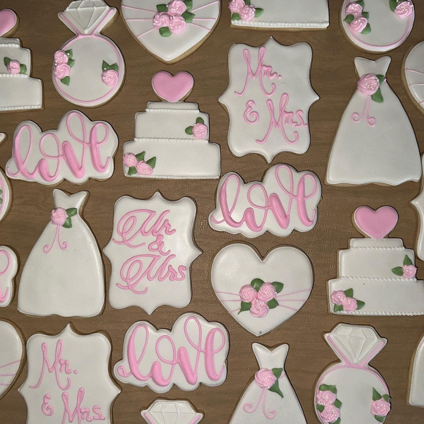White and pink cookies shaped like dresses, tiered cakes, hearts and rings, with script love plaques and piped roses