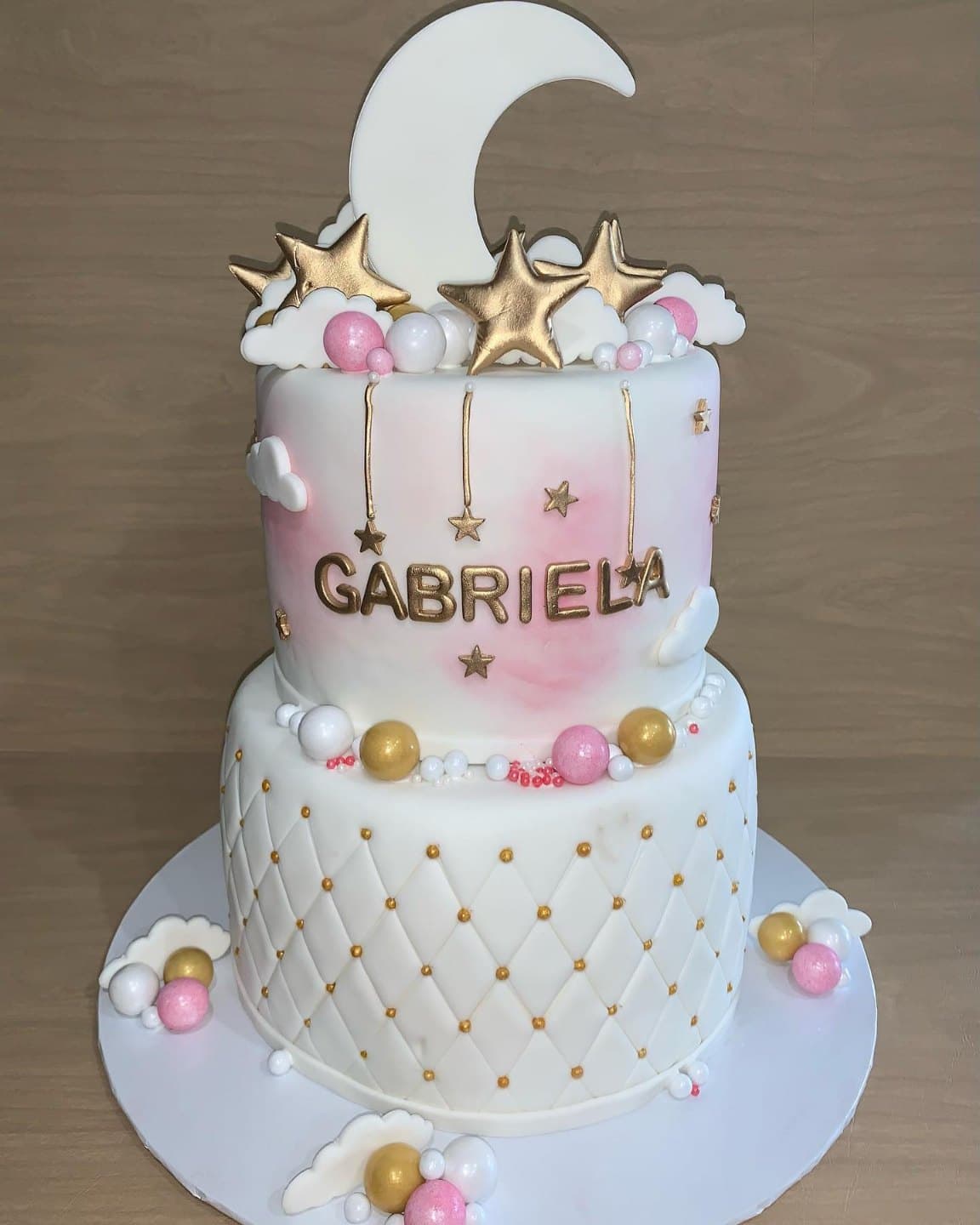 Two-tier cake with a quilted white bottom tier with gold pearls, a soft pink watercolor top tier and gold stars on top
