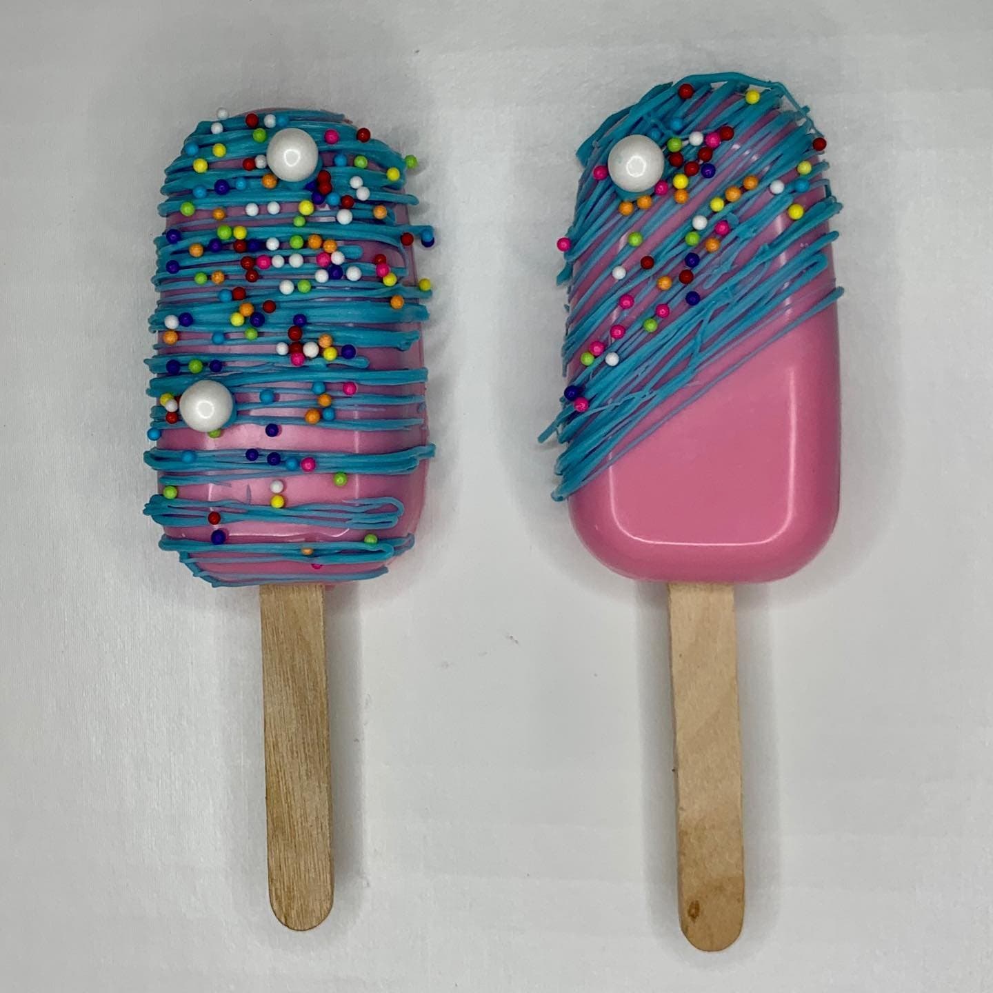 Two pink cakesicles with turquoise drizzle, rainbow sprinkles and sugar pearls