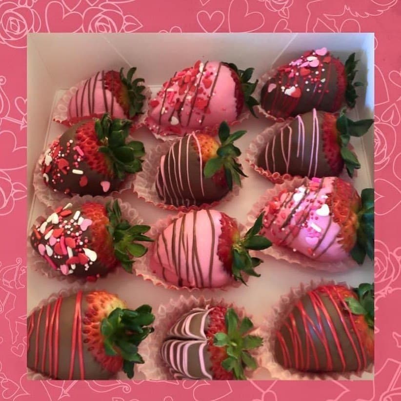 A dozen chocolate-dipped strawberries with pink and red drizzle in a gift box
