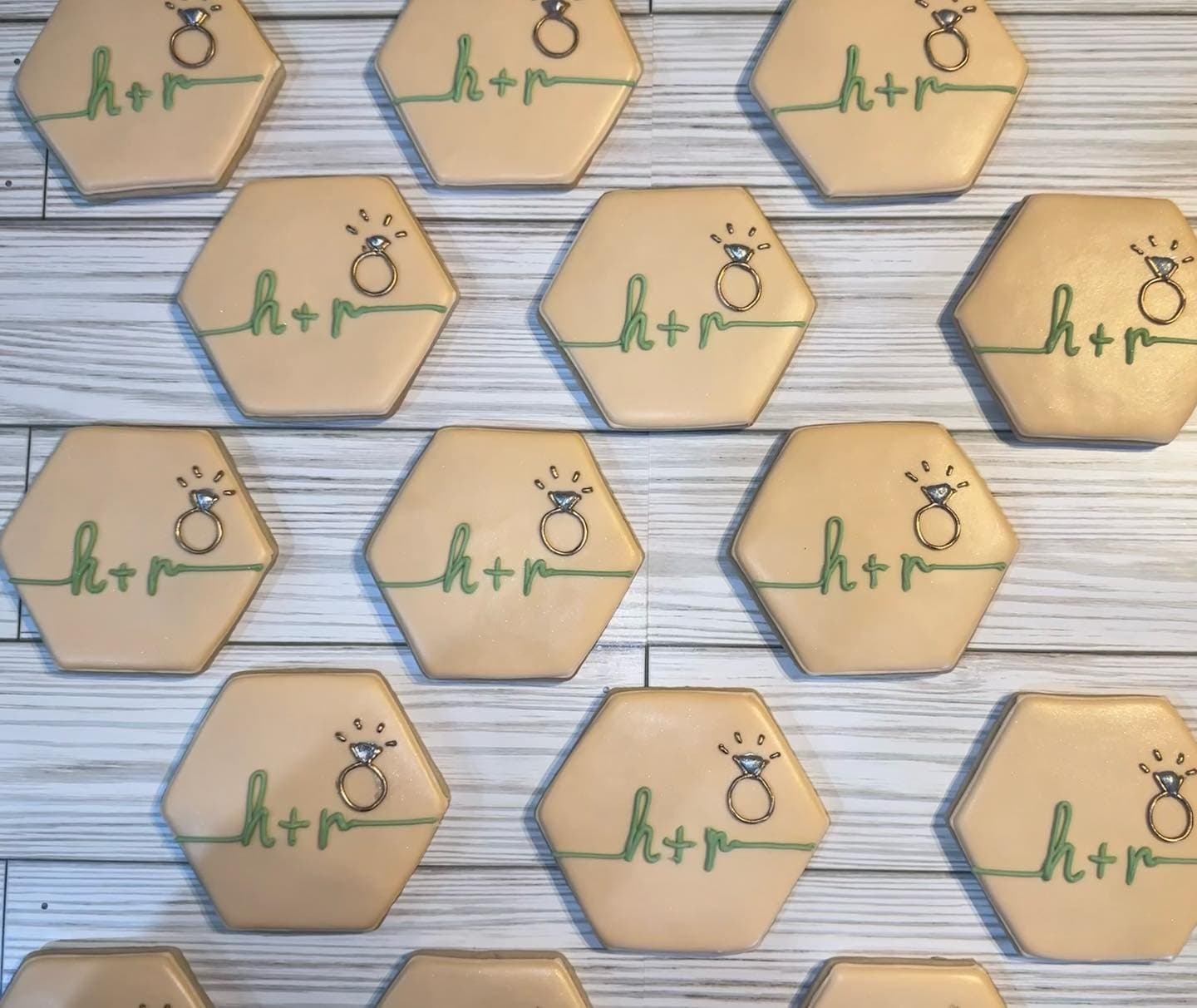 Rows of peach hexagon cookies with the couple's initials in green script and a tiny diamond ring