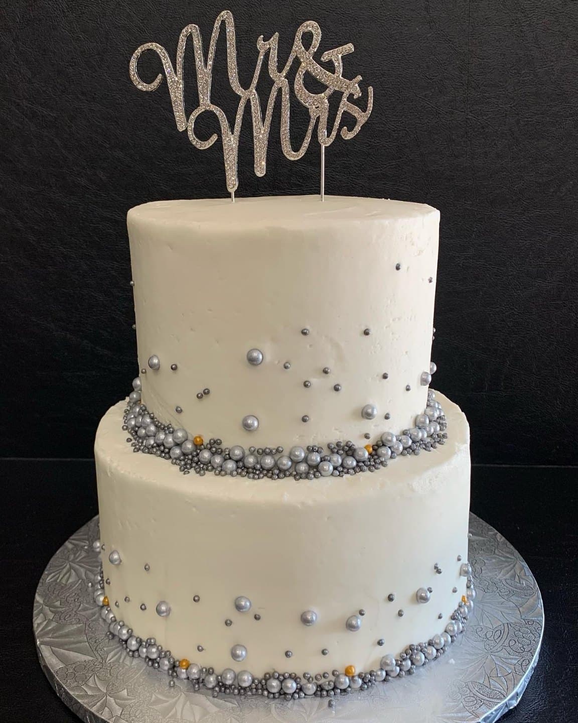Two-tier smooth white wedding cake with a band of silver sugar pearls and a sparkly Mrs topper